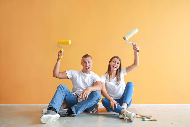 Felice giovane coppia con rulli di vernice seduto sul pavimento nella loro nuova casa
 - Foto, immagini