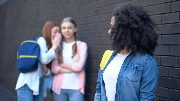 Afro-american female student looking at gossiping classmates behind, college - Photo, Image