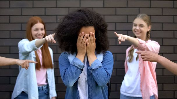 Humiliated black schoolgirl covering face hands, college peers pointing fingers - Valokuva, kuva