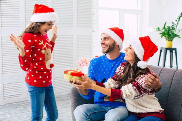 Mother and father in Santa hats giving daughter surprise gift for Christmas - Fotoğraf, Görsel