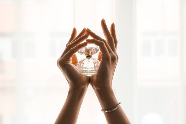 Руки красивой молодой женщины с бутылкой духов у окна
 - Фото, изображение