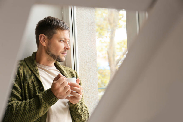 Чоловік з чашкою чаю, що розслабляється біля вікна вдома
 - Фото, зображення