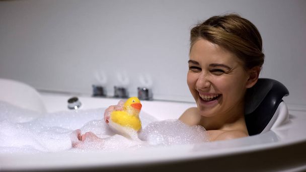 Positive woman playing with rubber duck in bath, childish mood, having fun - Photo, Image