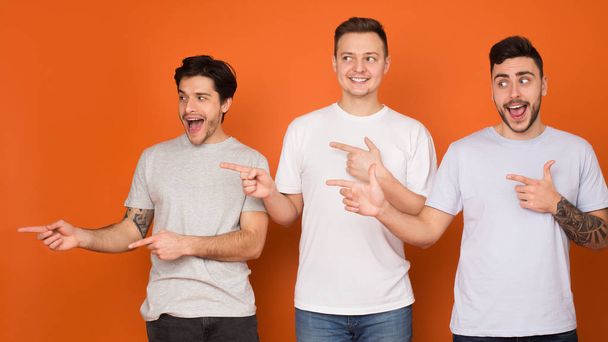 Excited guys pointing fingers away and looking aside, orange background - Photo, image