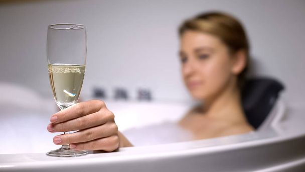 Elegant lady holding champagne glass in bath with foam bubbles, rest and relax - 写真・画像
