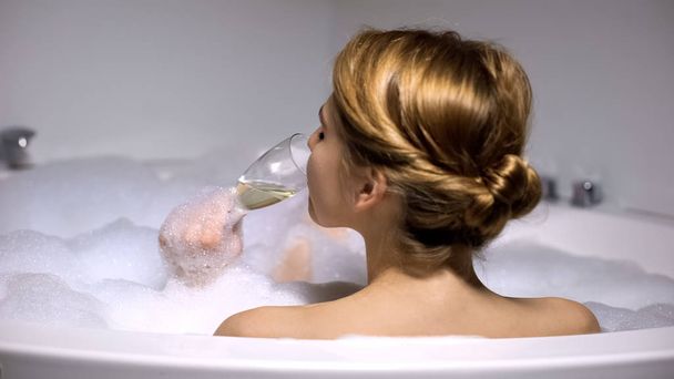Woman drinking champagne in bath with foam bubbles, spa chilling, back view - Photo, image