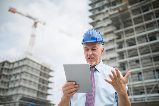 Site manager using his tablet in front of a construction site - Fotó, kép