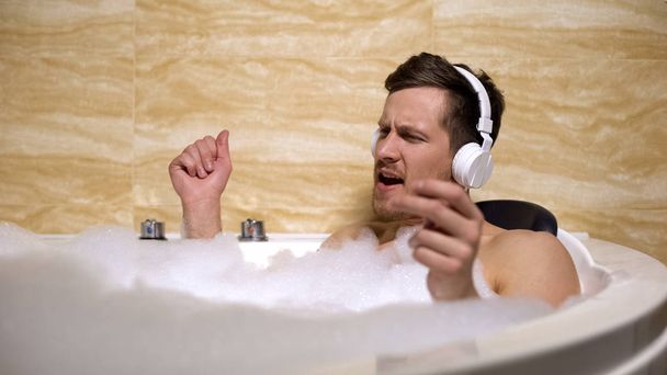 Active man in headphones taking bath with foam and moving to rhythm of music - Foto, Bild