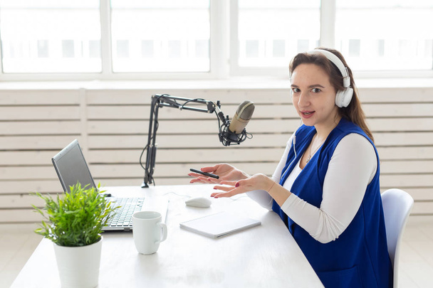 ラジオホストコンセプト - スタジオの白い背景の上にマイクの前に座ってラジオホストとして働く女性 - 写真・画像