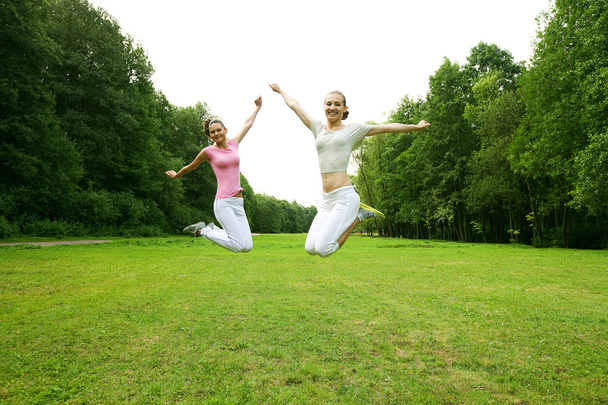 Two young girls jump in summer park. - Fotoğraf, Görsel