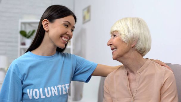 Frau im freiwilligen T-Shirt und Seniorin, die sich anschauen, sich umsorgen - Foto, Bild