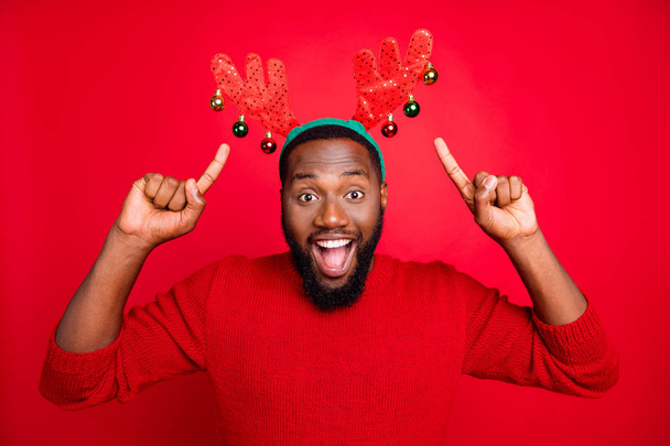 Theme night party concept. Portrait of astonished crazy man in stylish trendy pullover pointing at his deer toy costume recommending ads screaming wow omg isolated over red background - Photo, image