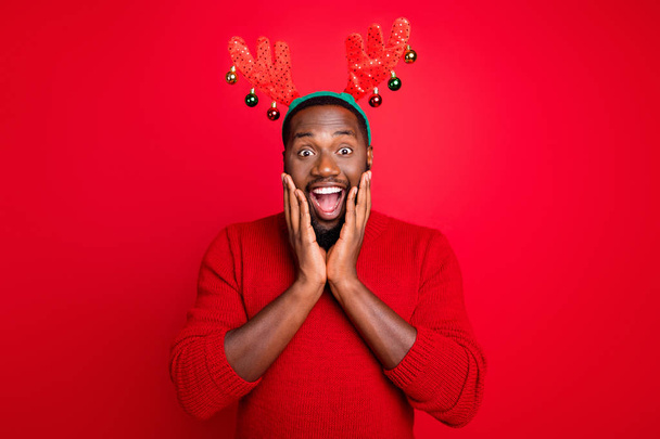 Portrait of impressed guy with black beard in fake deer costume screaming wow omg see desire present for x-mas wearing stylish fashion jumper isolated over red background - Fotoğraf, Görsel