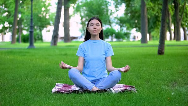 Menina atraente meditando no parque sentado postura de lótus, relaxando ao ar livre
 - Foto, Imagem