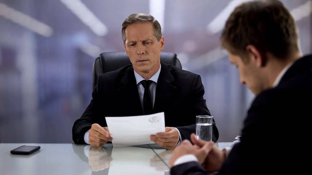 Nervous employee waiting for boss reading curriculum vitae, hoping for best - Photo, image
