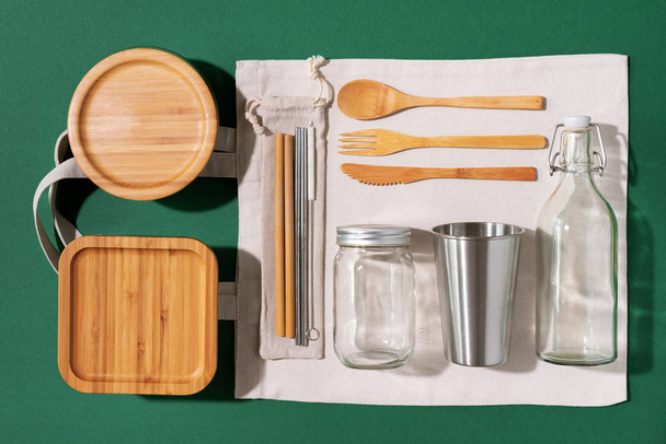 Sustainable lifestyle. Zero waste, plastic free shopping concept. Cotton bags, glass jar, bottle, metal cup, straws for drinking, bamboo cutlery and boxes on green background. - Foto, immagini