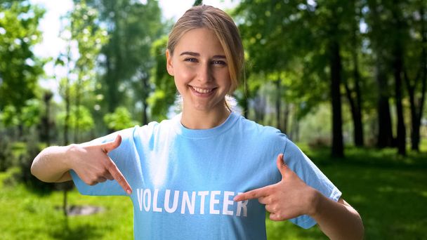 Smiling female pointing at volunteer word on t-shirt, forest conservation, earth - Фото, зображення
