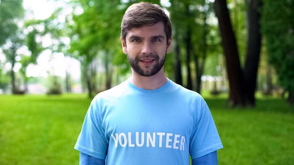 Усміхнений чоловік-доброволець у синій футболці, що стоїть на відкритому повітрі, готовий допомогти, благодійність
 - Фото, зображення