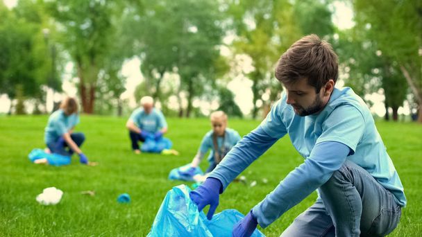 Male volunteer picking up litter and smiling on camera, eco project, activists - 写真・画像