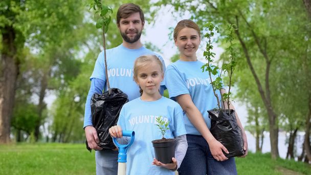 Parents and child in volunteer t-shirts holding potted trees nature conservation - Foto, Imagen