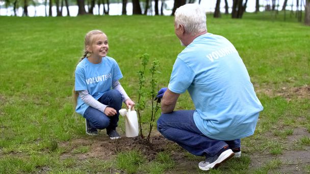 Mädchen freiwillige Gießkanne hilft Opa Baum pflanzen, einander lächelnd - Foto, Bild