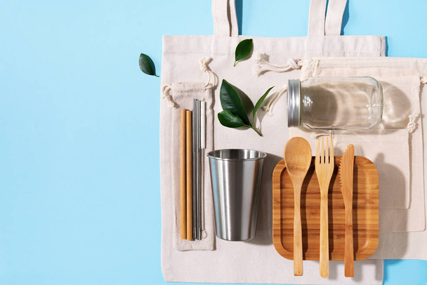 Sustainable lifestyle. Zero waste, plastic free shopping concept. Cotton bags, glass jar, bottle, metal cup, straws for drinking, bamboo cutlery and boxes on blue background - 写真・画像