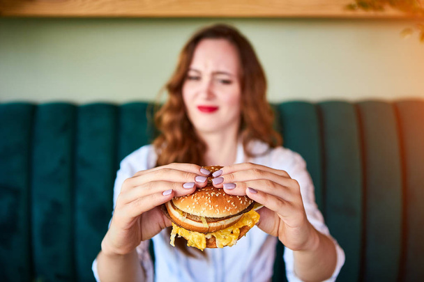 Mooie vrouw weigert ongezonde hamburger te eten. Ze kijkt het met afweerste - Foto, afbeelding