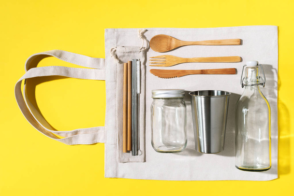 Cotton bags, glass jar, bottle, metal cup, straws for drinking, bamboo cutlery and boxes on yellow background. Sustainable lifestyle. Zero waste, plastic free shopping concept - Foto, Imagen
