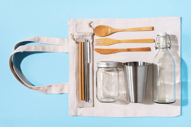 Cotton bags, glass jar, bottle, metal cup, straws for drinking, bamboo cutlery and boxes on blue background. Sustainable lifestyle. Zero waste, plastic free shopping concept - Foto, Bild