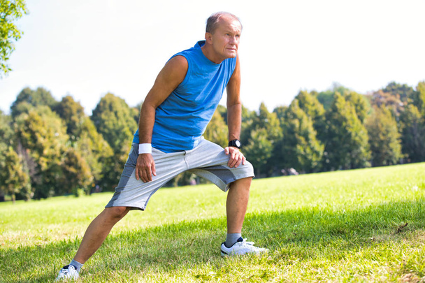 Active senior man stretching leg in park on sunny day - Photo, Image