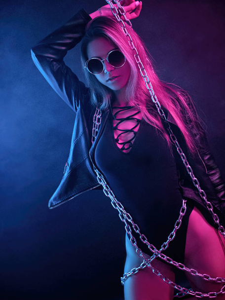 beautiful stylish fashionable girl in bodysuit posing in photo Studio on dark background with chains in neon light - Fotografie, Obrázek