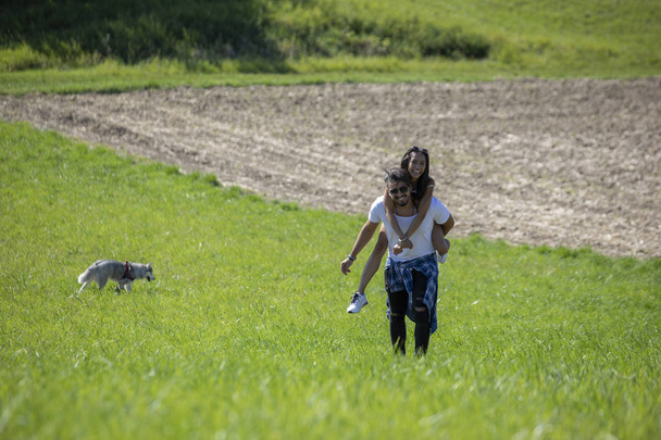 Ευτυχισμένο νεαρό ζευγάρι περπάτημα σε ένα χωράφι από γρασίδι και παίζοντας ξαναδώ ποτέ - Φωτογραφία, εικόνα