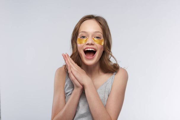 Happy teen girl using gold under-eye patches - Foto, afbeelding