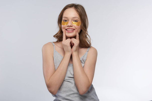 Cute teen girl in tank top using gold under-eye patches - Foto, Bild