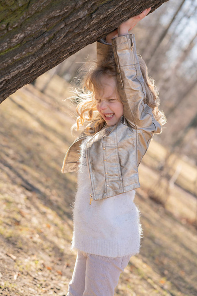 niña bastante rizado en chaqueta de cuero posando cerca de gran árbol en el parque de la ciudad solo
 - Foto, imagen