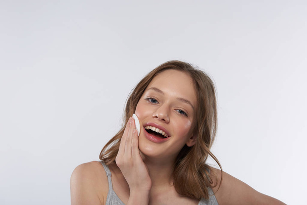 Charming teen girl using cotton pad and smiling - Fotó, kép