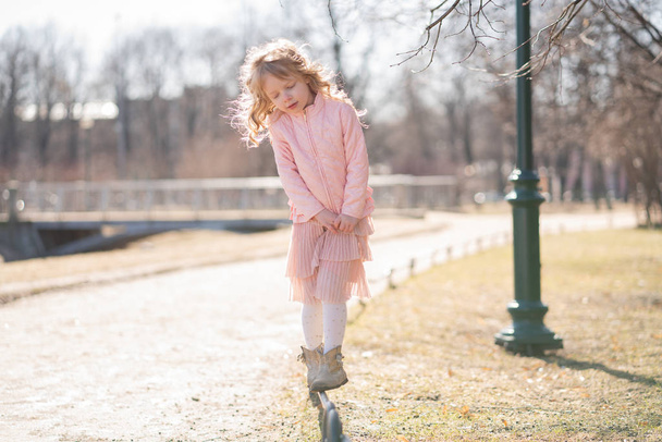 Pembe ceket, sevimli etek ve sıcak külotlu çorap Pretty mutlu kız tek başına şehir parkı güneşli bir günde kaldırıma gider - Fotoğraf, Görsel