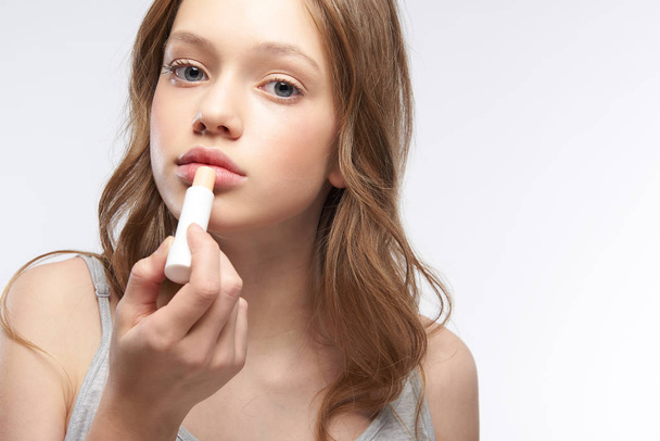 Charming teen girl with brown hair using hygienic lipstick - Fotó, kép