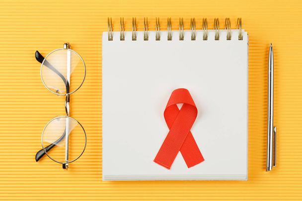 red aids ribbon on open notebook isolated on yellow background - Photo, Image