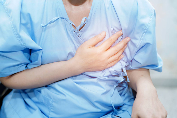 Азиатская женщина среднего возраста больная боль в груди может быть симптомом сердечного приступа в стационарном отделении: здоровая медицинская концепция
 - Фото, изображение