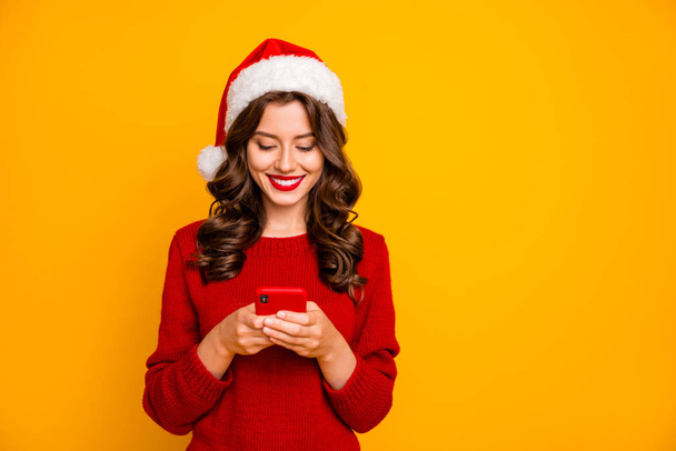 Fotografie úžasné dámy přidržující telefon v rukou nosí pletené pulovru a Santa Hat izolované žluté pozadí - Fotografie, Obrázek