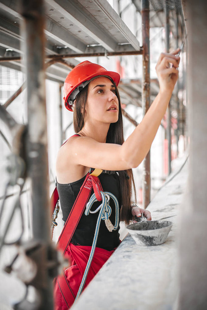 Female worker plastering old building wall using cement plaster mix  - 写真・画像