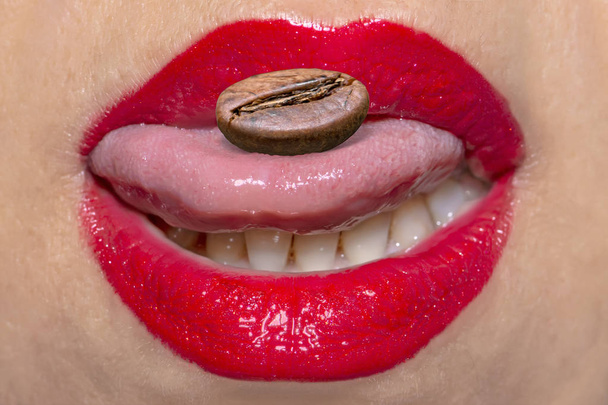 Blízký portrét ženských rtů s červeným make-upem a pražené kávové semeno na jazyku - Fotografie, Obrázek