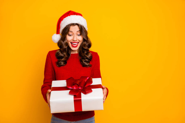 Pretty lady holding large giftbox in arms wear knitted pullover and santa hat isolated yellow background - Fotoğraf, Görsel