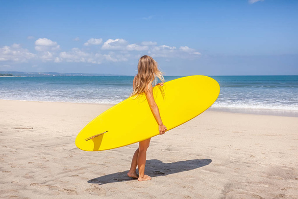 Back view of young woman with long hair holding the surfboard preparing to surf - Foto, imagen