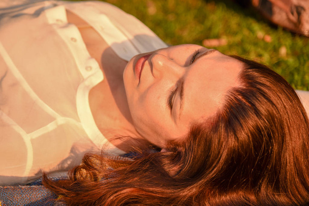 A beautiful red-haired woman lies on the ground with her head to the camera, her white shirt slightly unbuttoned. - Foto, Imagem