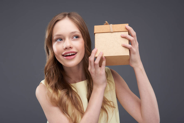 Beautiful teen girl shaking gift box and trying to guess what hidden inside - Photo, image
