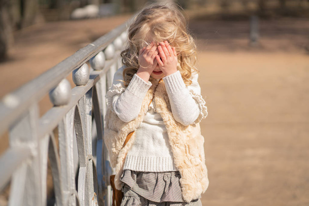 meisje sluit gezicht met haar handen en gelukkig speelt buiten - Foto, afbeelding