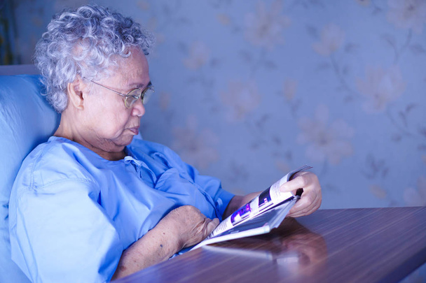 Азиатская пожилая или пожилая старушка-пациентка, читающая книгу, сидя на кровати в палате медсестер: здоровая сильная медицинская концепция
 - Фото, изображение
