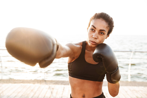 Image of athletic pretty woman training in boxing gloves by seas - 写真・画像